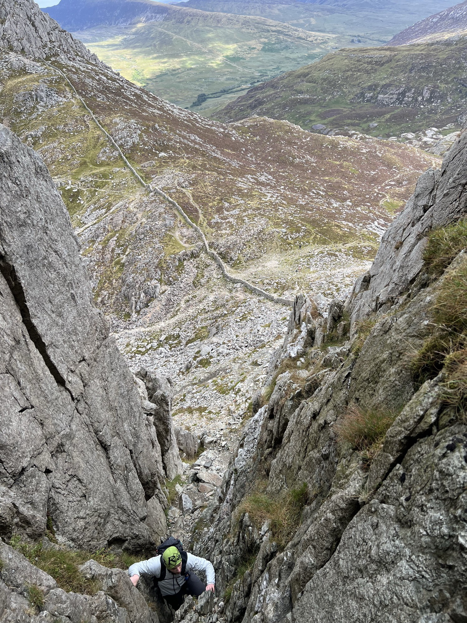 Ben scrambling up a steep rock gully, seen from above, with a valley far below.
